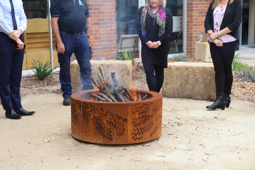 Fire pit alight with four people standing behind it.