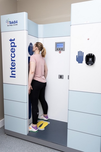 A woman stands facing forwards in the scanner, arms by her side, legs apart.