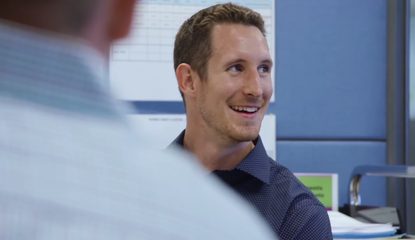 A person in a blue shirt looks to the side, smiling, in an office.