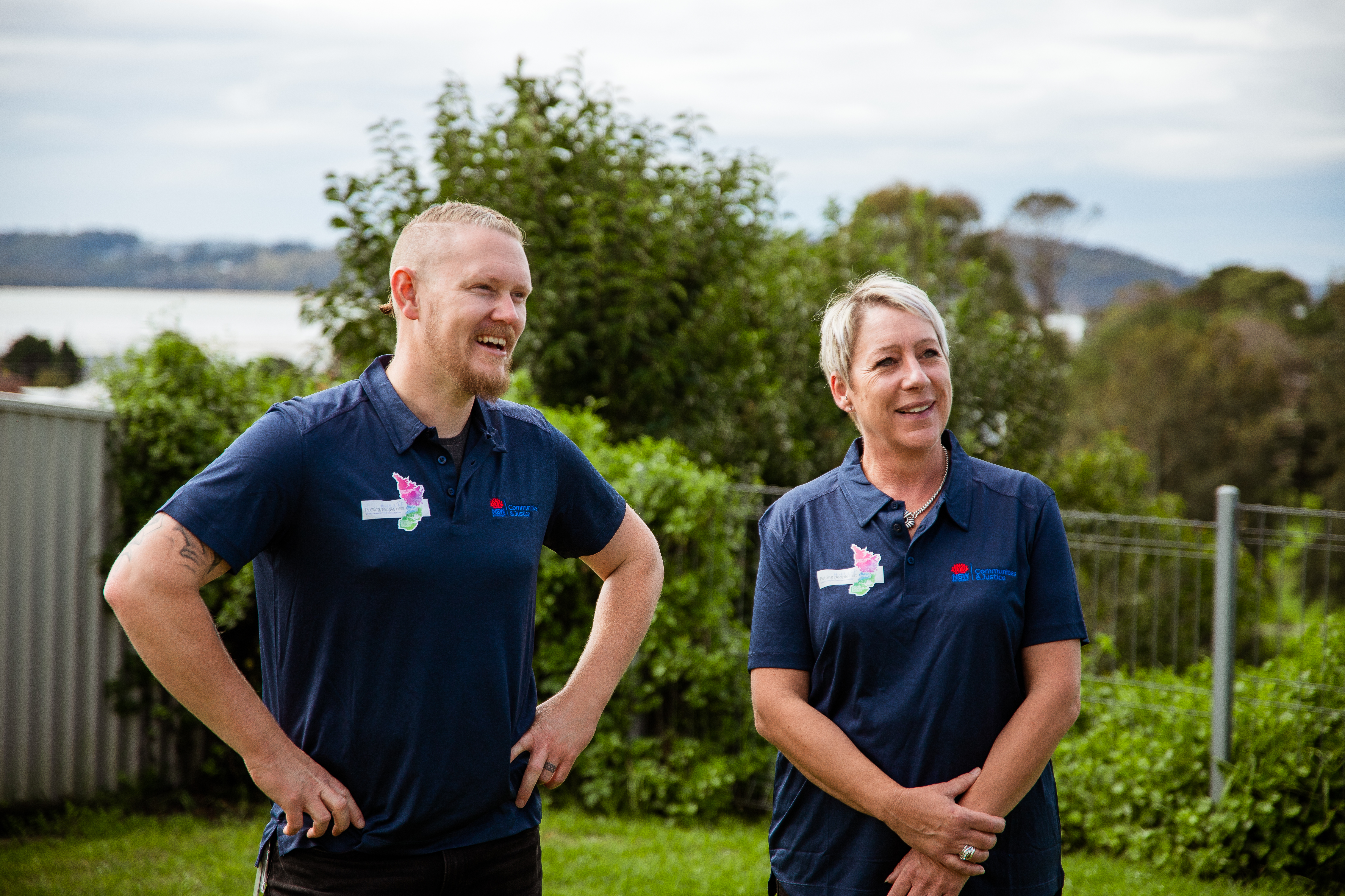 Two DCJ Housing staff members standing and smiling in a clients backyard