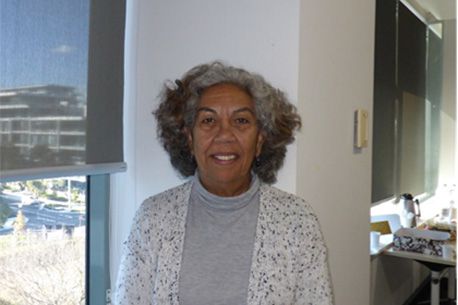 Portrait of Deborah Swan smiling at the camera wearing a grey turtleneck and a white cardigan