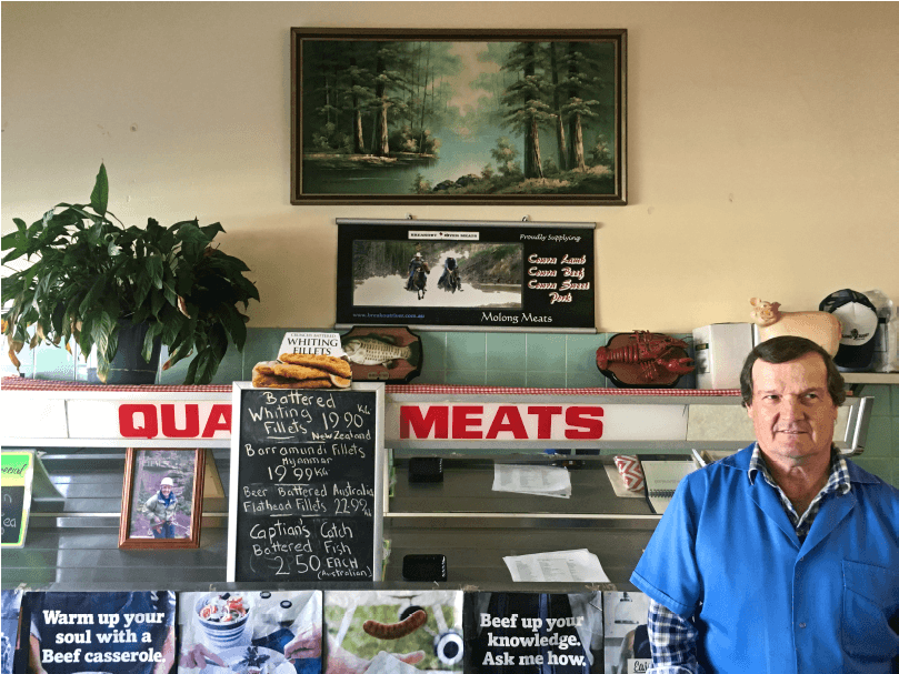 Tim stands in a butcher's shop with signs, pictures and ornaments relating to meat displayed beside and behind him.