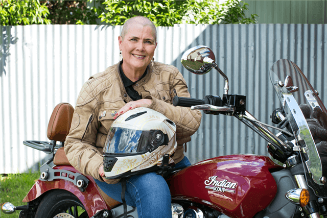 Janine sitting on her red Indian scout motor bike as she holds her helmet on her lap.