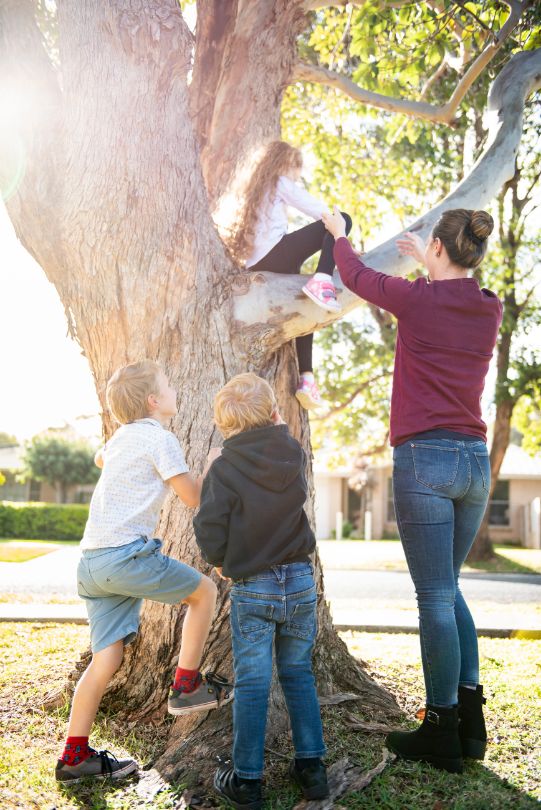 Ella helping her daughter come off a tree. Her two sons are standing next to the tree as well. 