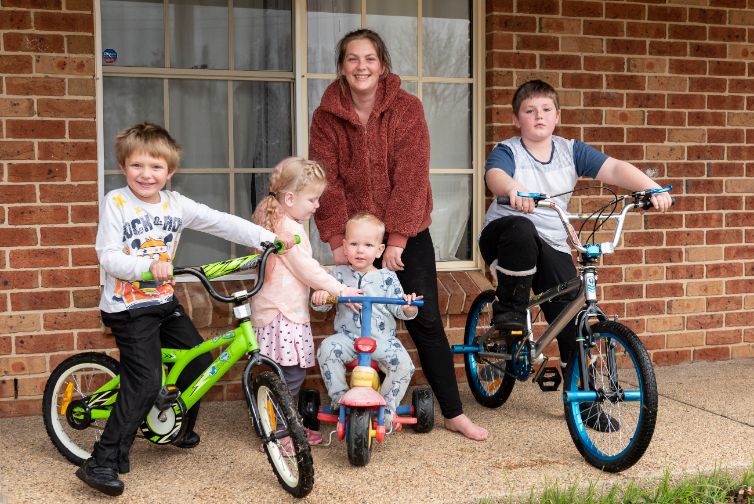 Kim and her four children photographed on their front porch. Her three sons are on bicycles. 