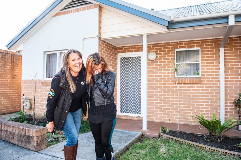 Tanya and Kate pictured laughing in front of a house.
