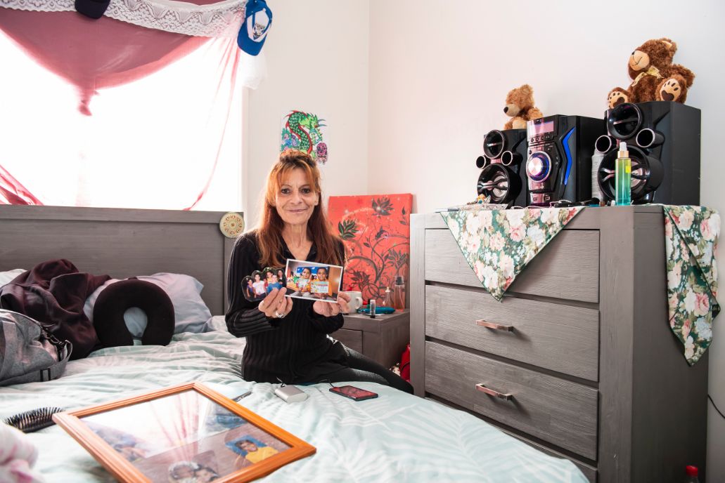 Tanya pictured sitting on a bed holding up printed pictures of her children to the camera.