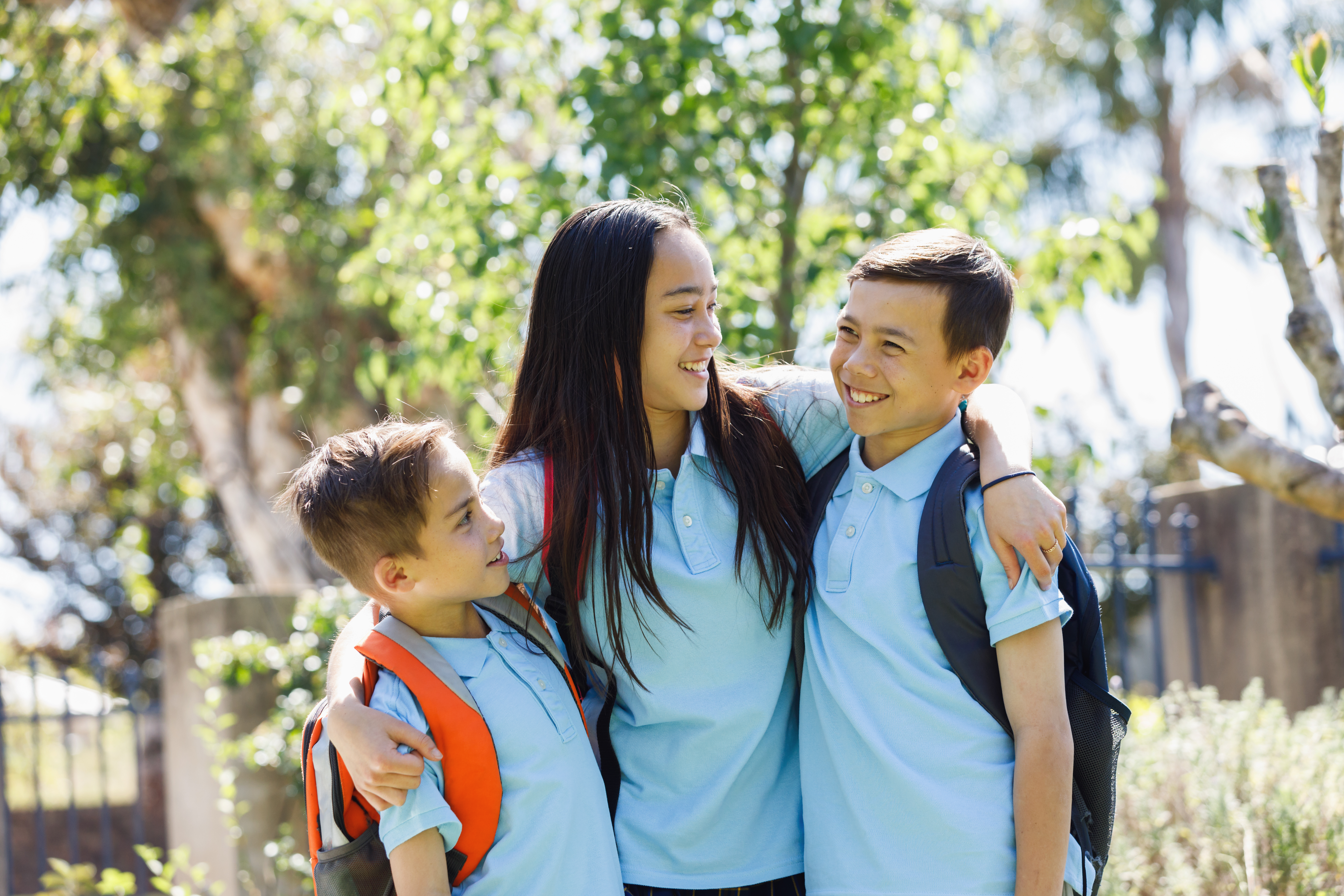 Three primary school children in uniform smiling and embracing.